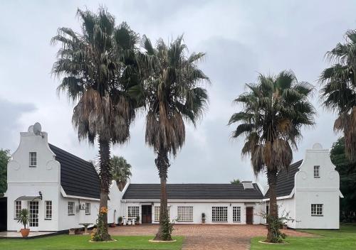 a white house with palm trees in front of it at Madeley House Unit 2 near Oliver Tambo Airport in Boksburg