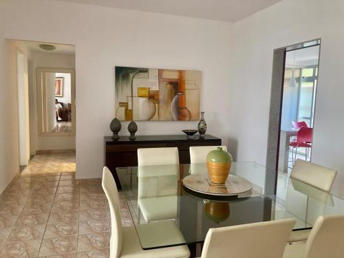 a dining room with a glass table and white chairs at Conforto e espaço - 3 quartos, 3 vagas e a 150m do mar in Guarapari