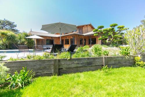 a house with an umbrella in a yard at Villa Palombes au Cap Ferret charming villa with swimming pool in Cap-Ferret