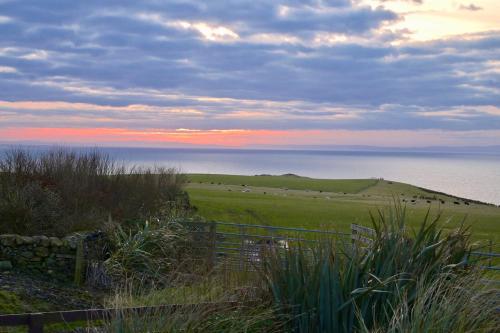een uitzicht op een veld met een hek en de oceaan bij Amazing Sunsets and Sea Views - Lodge Cabin Farm Stay - Caol Ila - Lodge 8 in Stranraer