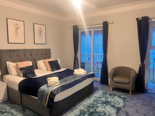 a bedroom with a bed and a chair and windows at Seaside Escape in Thorpe Bay