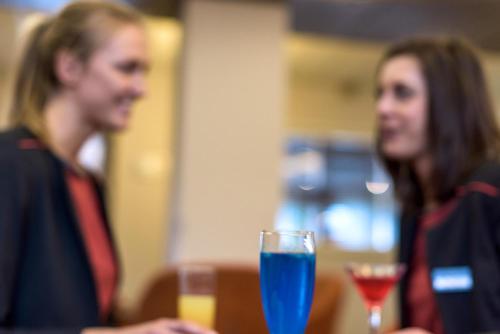 two women sitting at a table with a blue drink at Clarion Aparthotel Toulouse Le Parc de l'Escale in Toulouse