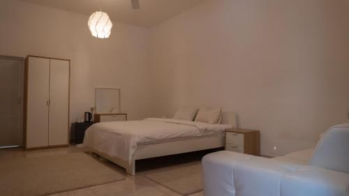 a white bedroom with a bed and a couch at بيت الشّاب Al Shab House in Ţīwī
