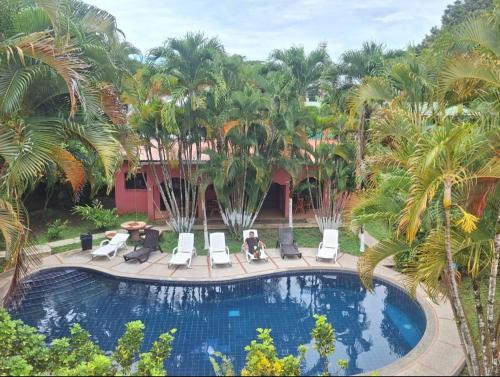 a pool with chairs and palm trees in front of a building at Hotel El Paraiso Escondido - Costa Rica in Jacó
