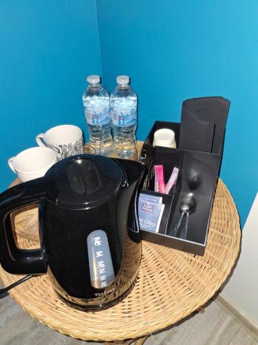 a tea kettle on a wicker table with a box of water at 2 chambres d'hôtes in Wissous