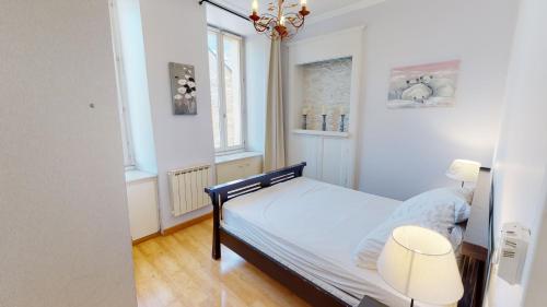 a bedroom with a bed and two windows and a chandelier at Les Meublés d'Etigny in Luchon