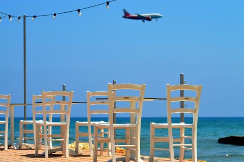 a row of white chairs on the beach with an airplane at Island Boutique Hotel in Larnaka