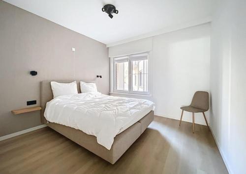 een witte slaapkamer met een bed en een stoel bij Apartment Sunset Koksijde in Koksijde