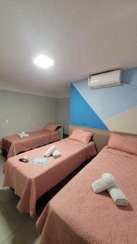 a room with three beds with pink sheets at Pousada Sol e Descanso by Easy Hotéis in Arraial do Cabo