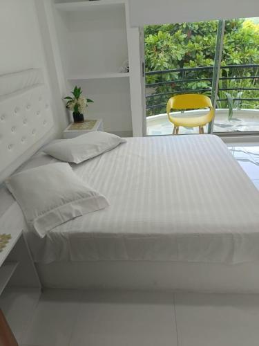 a white bed with a yellow chair in a bedroom at Casaquinta Con Piscina in Villeta