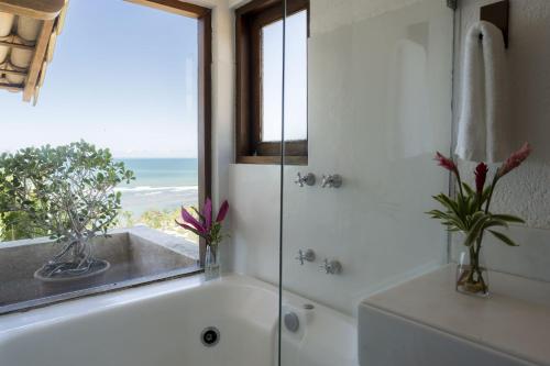 a bathroom with a bath tub and a window with the ocean at Hotel Maitei in Arraial d'Ajuda