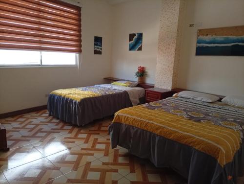 a bedroom with two beds and a window with a window blindiosyn at Hostal Shaddai in Manta