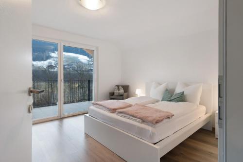 a white bedroom with a bed and a large window at Talferblick in Sarntal