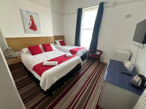a bedroom with two beds with red pillows and a television at Tuxford House in Blackpool