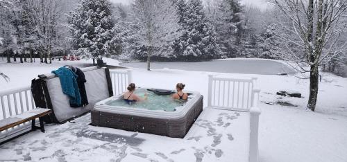 2 personnes assises dans un bain à remous dans la neige dans l'établissement Mountain Blue Vista - Luxury retreat near Ski resorts with Pond, Firepit and Hot Tub, à Windham