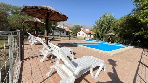 a group of white chairs and an umbrella next to a pool at Cabañas Aldea Blanca in Merlo