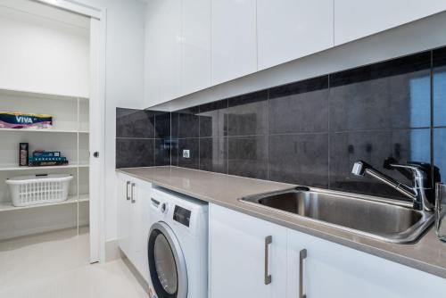 een keuken met een spoelbak en een wasmachine bij Luxury Pool Home Near Noosa & Coolum Sleeps 8 in Peregian Springs