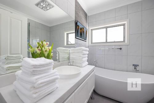 y baño blanco con bañera, lavabo y toallas. en Luxury Waterfront Getaway, en Toukley