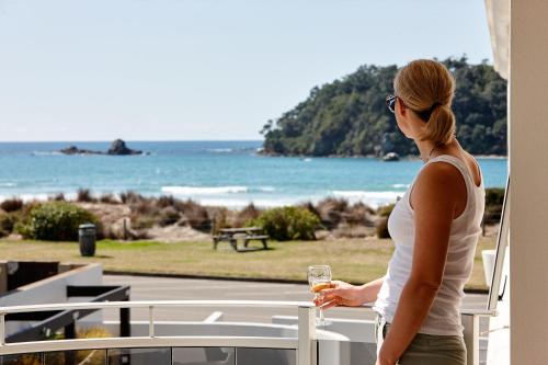 a woman standing on a balcony with a glass of wine at Belle Mer Beachfront Apartments in Mount Maunganui