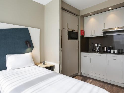 a bedroom with a white bed and a kitchen at Aparthotel Adagio London Stratford in London