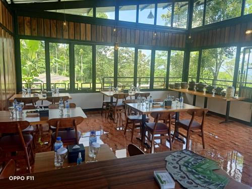 een restaurant met tafels, stoelen en ramen bij Menoreh Farm Stay Samigaluh Kulonprogo in Kalirejo