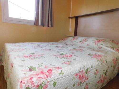 a bed with a white blanket with pink roses on it at CAMPING de la BUGE in Rochefort-Montagne