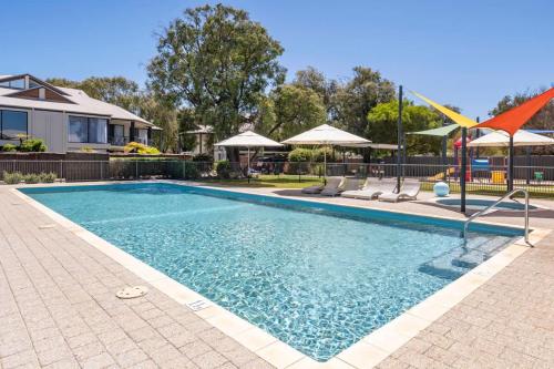 a swimming pool with chairs and umbrellas next to a house at 63@CapeView, Geographe bay in Busselton