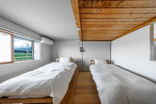 two beds in a room with two windows at Peace Garden Furano in Nakafurano