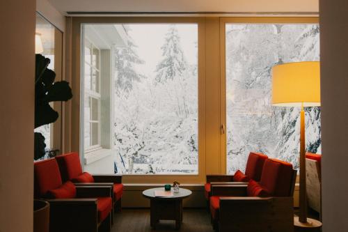 a room with a large window with red chairs and a table at Grand Hotel Belvedere, a Beaumier Hotel in Wengen