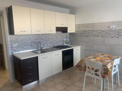 - une cuisine avec des placards blancs, un évier et une table dans l'établissement Appartamenti STELLA MARINA- Posto Rosso, à Alliste