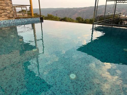 a large swimming pool with blue water and mountains in the background at Savitri villa inn in Mahabaleshwar