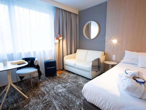 a hotel room with a bed and a chair and a desk at Novotel Mulhouse Bâle Fribourg in Sausheim