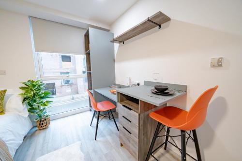 una piccola cucina con sedie arancioni e una scrivania in una stanza di URBAN HUB Student Accommodation a Preston