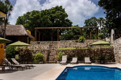 una piscina con sillas y sombrillas junto a una pared de piedra en Hotel Rinconada del Convento, en Izamal