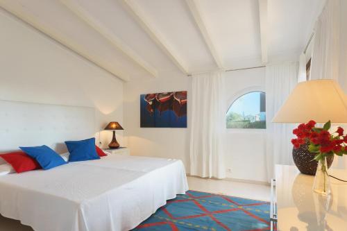 een witte slaapkamer met een bed en een vaas met bloemen bij Playa in Port de Pollença
