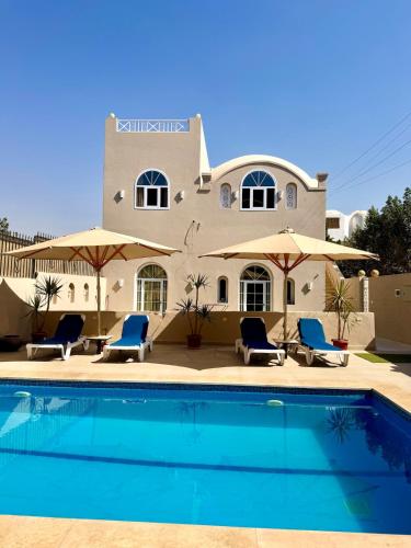 a house with a swimming pool with chairs and umbrellas at Royal Home Dome Style - Ground Floor Apartment in Jazīrat al ‘Awwāmīyah