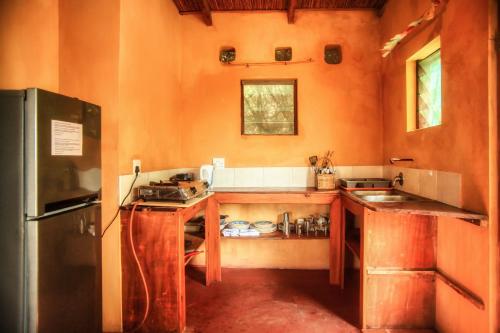 Tree House Cottage, Ocean View في بارايا دو توفو: مطبخ بجدران برتقالية وثلاجة وطاولات