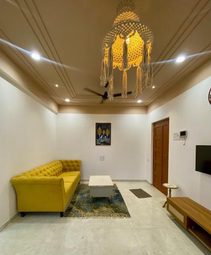 a living room with a yellow couch and a chandelier at Go-kul Homestay in Kolhapur