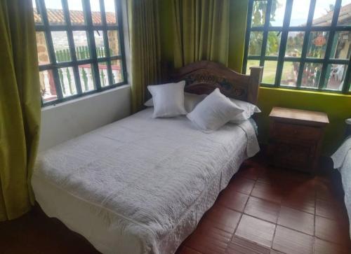 une chambre avec un lit avec des draps blancs et des fenêtres dans l'établissement POSADA VILLA DEL ROSARiO, à Sutamarchán