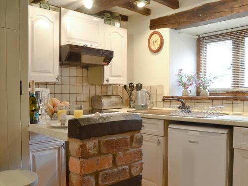 a kitchen with white cabinets and a brick wall at Lower Barn in Wistanstow