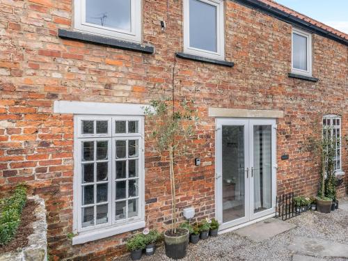 a brick house with white windows and potted plants at Warrington Mews-Uk48821 in Thornton Dale