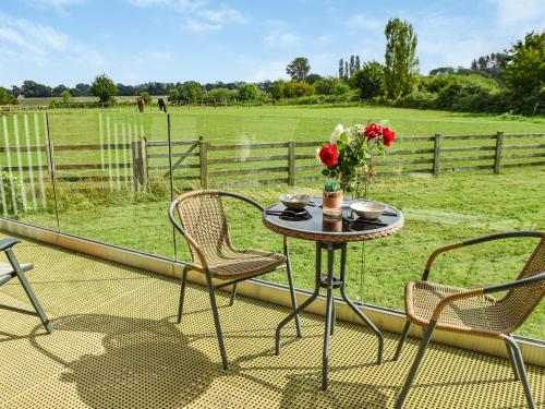 a table with a vase of flowers on a balcony with a field at Cedar Lodge in Old Buckenham