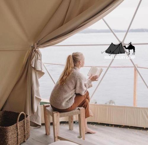 a woman sitting on a stool reading a book in a tent at MIRA LUXURY CAMp in Wadi Rum