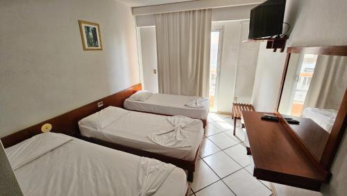 Una habitación de hotel con dos camas y un escritorio. en Atlântico Sul Renascença Hotel, en Laguna
