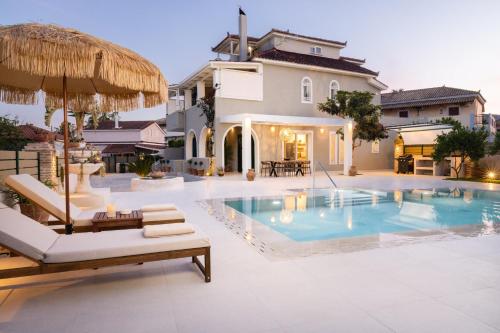 a villa with a swimming pool with chairs and an umbrella at Porta Verde Luxury Residence, By TK Premium Stays in Laganas