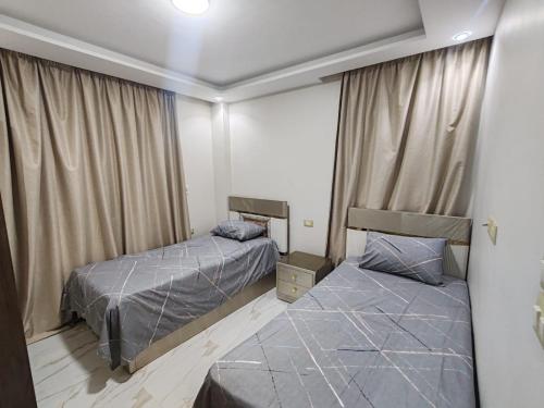 a bedroom with two beds and a window with curtains at First 6th October Compound of Degla Gardens Comfort in ‘Ezbet `Abd el-Ḥamîd