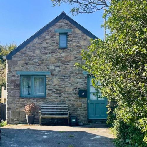 ein Steingebäude mit einer grünen Tür und einer Bank in der Unterkunft Bramble Cottage in Saint Columb Minor