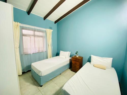 Habitación azul con 2 camas y ventana en Starlight Guest house, en Durban