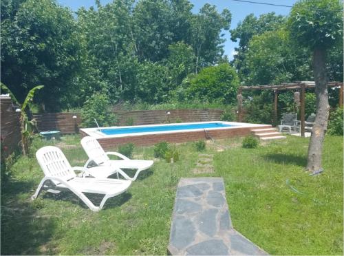 two white chairs sitting in the grass near a pool at Mí Cabaña in Chascomús