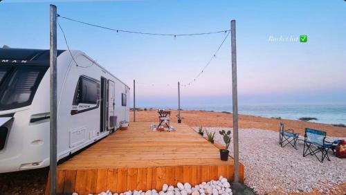 an rv parked on the beach with a wooden boardwalk at Flamingo Caravan in Ash Shāb